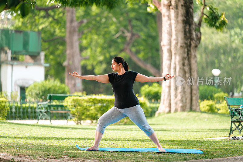 亚洲/印度女性在公园表演瑜伽体式，战士两种练习或Virabhadrasana II。